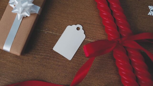 Brown gift box with white ribbon, red candles tied with ribbon, empty tag on wood