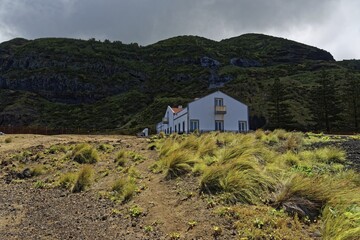 White house and thermal bath at the foot of a green lava mountain under a cloudy sky, Termas da Ferraria, Sao Miguel Island, Azores, Portugal