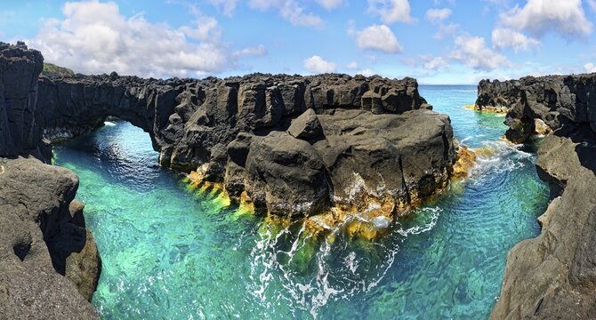 Rugged lava rock formations with a natural arch over a turquoise sea under a blue sky, A Porta do Diabo, Sao Miguel Island, Azores, Portugal