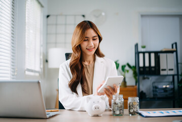 Asian woman saving for retirement Saving money through a piggy bank and taking notes in modern office
