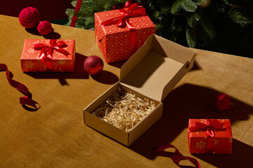A wooden table scene with an open kraft gift box and several red presents around it. The soft Christmas ornaments add charm, creating a friendly festive atmosphere.