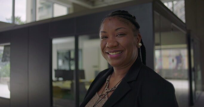African American woman smiling warmly standing near glass office wall conveying friendliness confidence and approachability in professional workplace setting