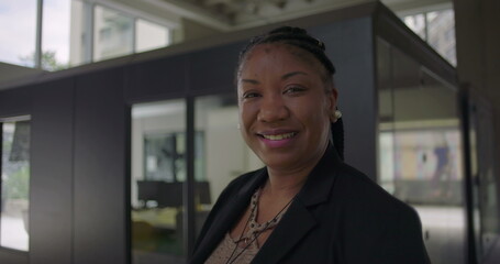African American woman smiling warmly standing near glass office wall conveying friendliness confidence and approachability in professional workplace setting