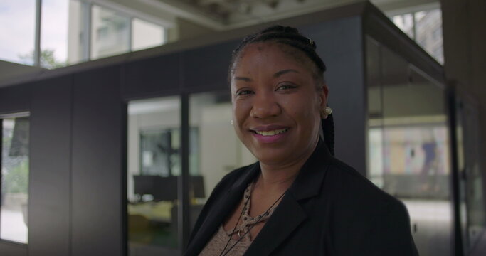African American woman smiling warmly standing near glass office wall conveying friendliness confidence and approachability in professional workplace setting