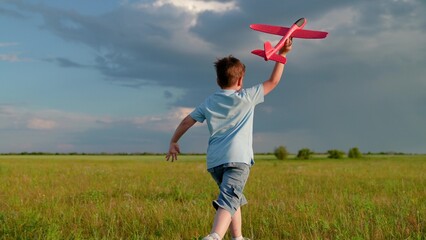 Cheerful boy dream of fly plane to travel. Child pilot play an airplane in green meadow. Happy boy play with toy airplane in spring meadow against sky, slow motion. Child holds an airplane in his hand © Victoriia