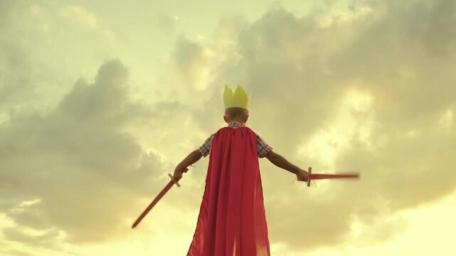 child superhero game sunset. red cape childish fantasy. countryside. golden crown head kid. achieve victory success. schoolboy plays sword. happy child superman red raincoat nature. concept happy