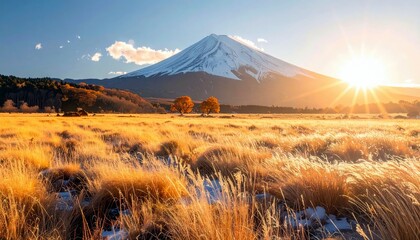 A majestic snow-capped mountain stands tall against a bright sunrise, with a field of golden grasses and autumn trees in the foreground.