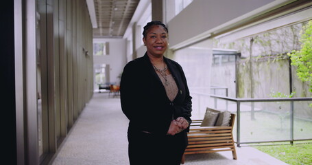 African American woman standing in office hallway with hands together smiling gently conveying warmth approachability leadership and trust in business context