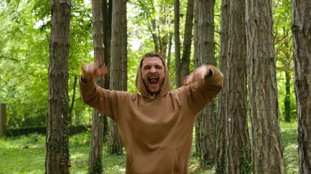 A man jumps energetically on a forest path, raising his hands in a rock gesture with an open-mouth expression of excitement. Concept highlights joy, freedom, energy and bold self-expression