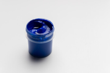 A jar of colored blue gouache on a white background. Copy space. A transparent jar of colored water-soluble paint.