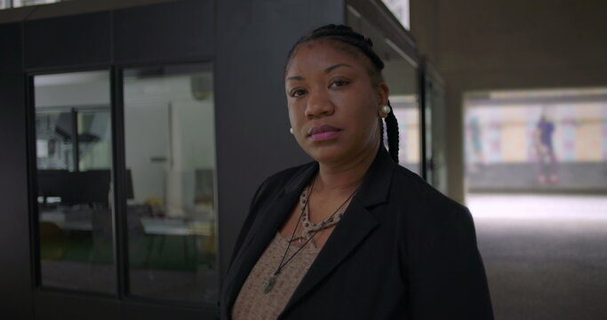 African American woman standing near glass office wall with serious expression looking confident composed and determined in modern workplace environment - Powered by Adobe