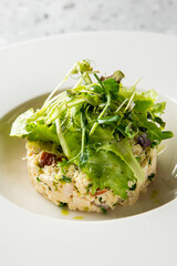 Gourmet crab and avocado salad stack with fresh microgreens, served elegantly on a white plate in a fine dining restaurant