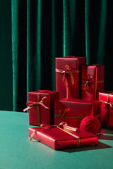 Several shiny red Christmas presents stacked together on a green table with a dark curtain...