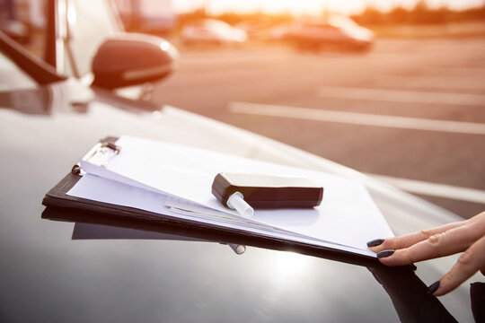 Female Hand Touches Clipboard With Alcohol Tester On Car. Sobriety Check Procedure At Sunset.