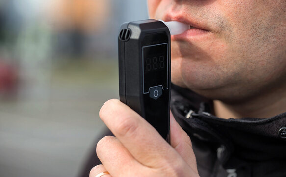 Male Driver Using Personal Alcometer For Sobriety Check. Man Exhaling Into Alcohol Test Device. Driving license revocation for alcohol