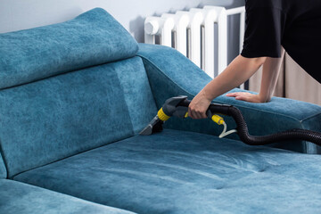 Cleaning a blue fabric couch with a vacuum cleaner during a home maintenance session