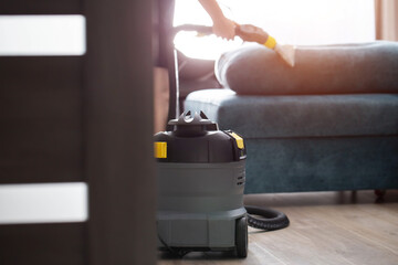 A modern upholstery vacuum cleaner stands in a room against a sunset backdrop. Cleaning service....