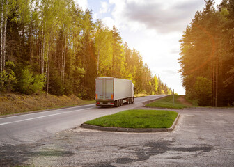 A truck with a semi-trailer transports cargo uphill in nature against the backdrop of a forest and...