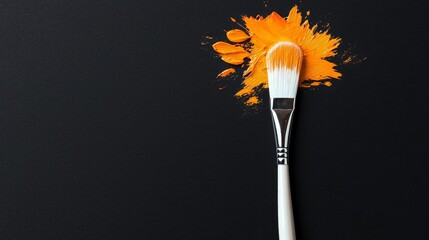 A clean paintbrush with white bristles is positioned over a dynamic splatter of bright orange paint on a black surface, suggesting creativity and artistic expre