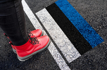 a woman with a boots standing on asphalt next to flag of Estonia and border
