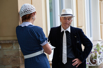 The conversation between the elderly stylish man and the woman in vintage clothes near the building on a sunny day