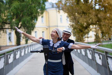 Couple joyfully riding a scooter together on a bridge during a sunny day in a beautiful park setting
