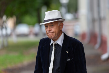 Stylish older man walks down the street wearing a hat and suit, capturing a moment of sophistication and reflection