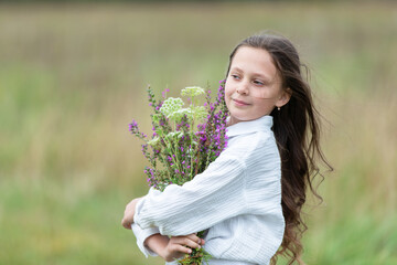 Young girl holds a bouquet of wildflowers in a green field during a sunny day