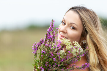 Woman with long hair holds a bouquet of wildflowers in a serene outdoor setting during the day