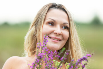 Smiling woman holding colorful flowers in a green field during a bright day in summer