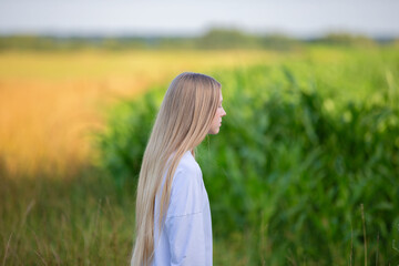 Young woman with long hair stands in a field during golden hour, reflecting on nature and solitude