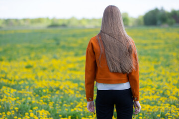 A woman with long hair walks away in a vibrant yellow flower field. The scene is bright and cheerful, showcasing the beauty of nature and warm weather in springtime.