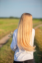 Long blonde hair flows gently as a person walks along a rural path in a sunny field, enjoying nature and solitude in the afternoon light