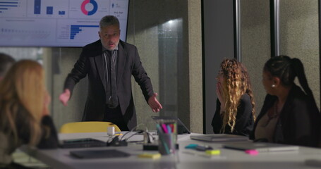 Angry business executive yelling during office meeting with team as colleagues react in shock near data screen in boardroom