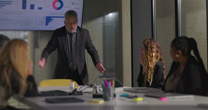 Angry business executive yelling during office meeting with team as colleagues react in shock near data screen in boardroom