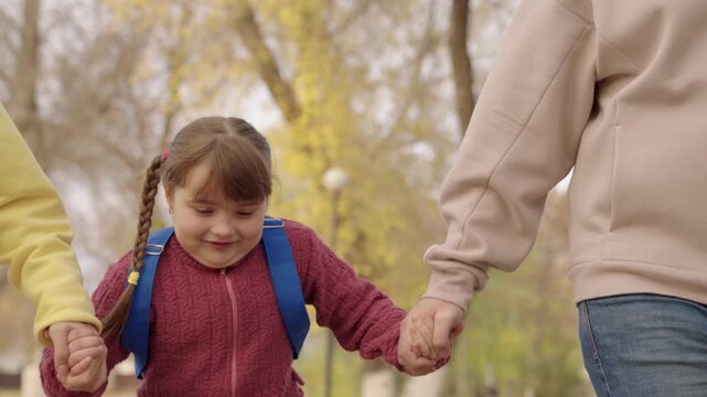 happy kid girl runs with her mother and father in city park, happy family life, cheerful child with backpack rushes to school in schoolyard, time to study and get an education, daughter with parents.