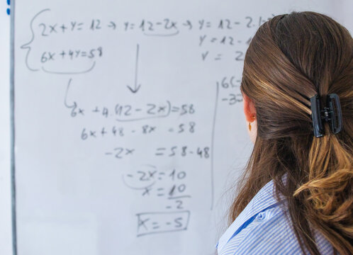 Teacher explaining complex algebraic equations on whiteboard during a math lesson, instructing students on solving problems and understanding mathematical concepts in education environment