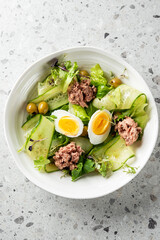A fresh and healthy tuna salad served in a white bowl, featuring chunks of flaked tuna, crisp lettuce, cucumber ribbons, green olives, and soft-boiled eggs