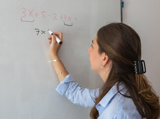 Young female teacher writing a math equation on a whiteboard in a classroom, demonstrating problem solving skills and dedication to education during a lesson