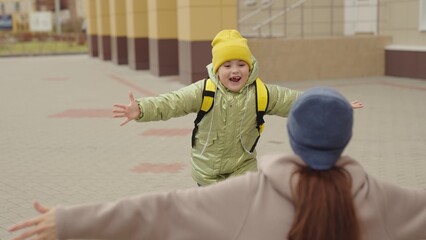 little girl schoolgirl with backpack runs hug her mother, kid rejoice over lessons, happy family, school bag behind back cheerful laughing child, baby hurries her mother her arms, jogging school yard.