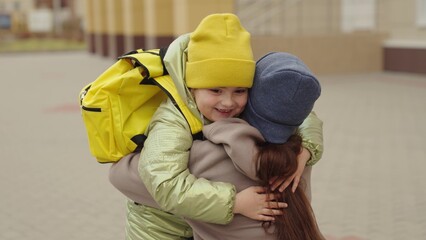 little girl schoolgirl with backpack runs hug her mother, kid rejoice over lessons, happy family, school bag behind back cheerful laughing child, baby hurries her mother her arms, jogging school yard.
