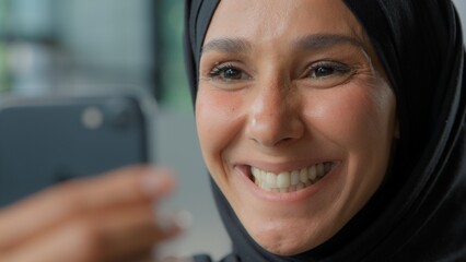 Portrait happy arabian business woman in hijab smiling looking in phone laughing smile Muslim businesswoman female girl with smartphone app carefree emotional joyful look in mobile smartphone email