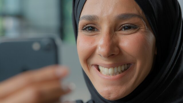 Portrait happy arabian business woman in hijab smiling looking in phone laughing smile Muslim businesswoman female girl with smartphone app carefree emotional joyful look in mobile smartphone email