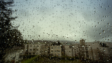 Rain drops flowing down a large home window. Close up, ultra wide angle macro shot, buildings in...