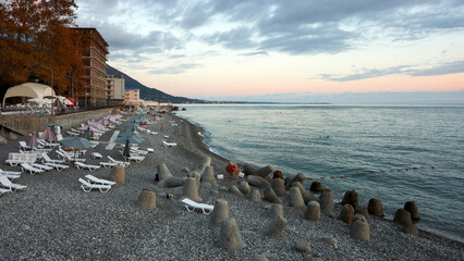 The seashore in Old Gagra. A pebble beach with sun loungers, umbrellas, breakwaters, and a few sunbathers at sunset.