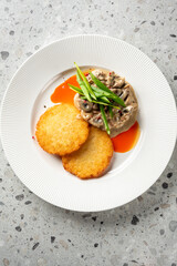 two golden-brown potato pancakes served on a white plate with a creamy mushroom sauce and green onion garnish on a speckled grey surface.