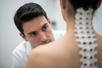 A close-up view of a male medical professional, such as an orthopedist or chiropractor, examining the back of a female patient in a clinic.