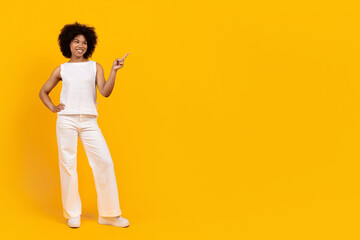 Full body portrait of confident young African American woman standing and pointing aside on yellow background. Space for text or promotional content