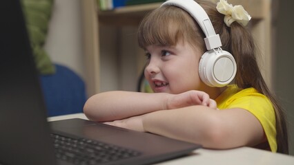 little schoolgirl headphones does homework while sitting digital laptop. distance learning online students. children funny communication through internet video communication. lessons monitor display