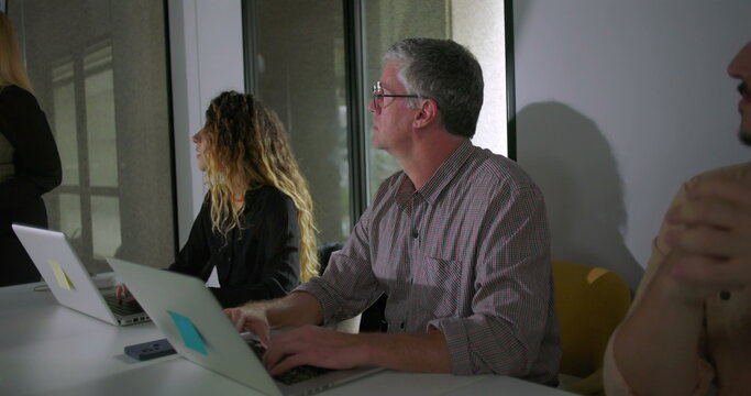 Blonde businesswoman explaining data with hand gestures as colleagues listen during team meeting in glass walled office with charts on screen